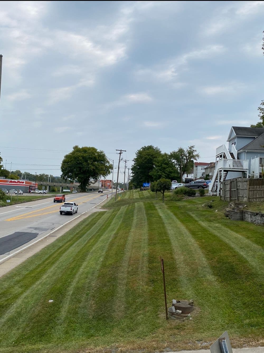 Striped green lawn along a road with trees and houses in the background.