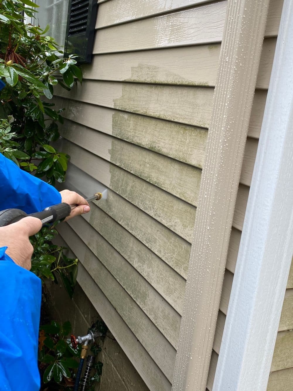 Person cleaning mold off house siding with pressure washer on a rainy day.