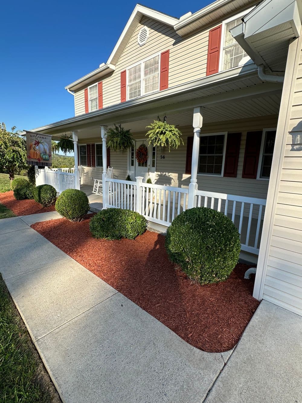 Charming house with white porch, red shutters, and landscaped front yard in daylight.