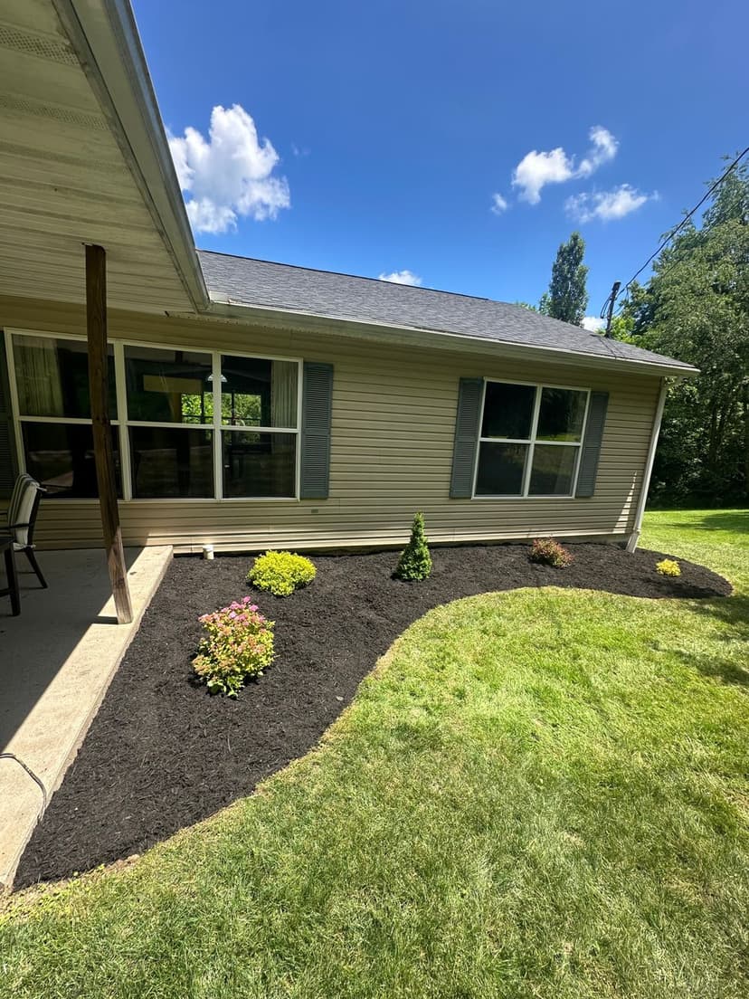 Lush green lawn with landscaped flower beds near a house and clear blue sky.
