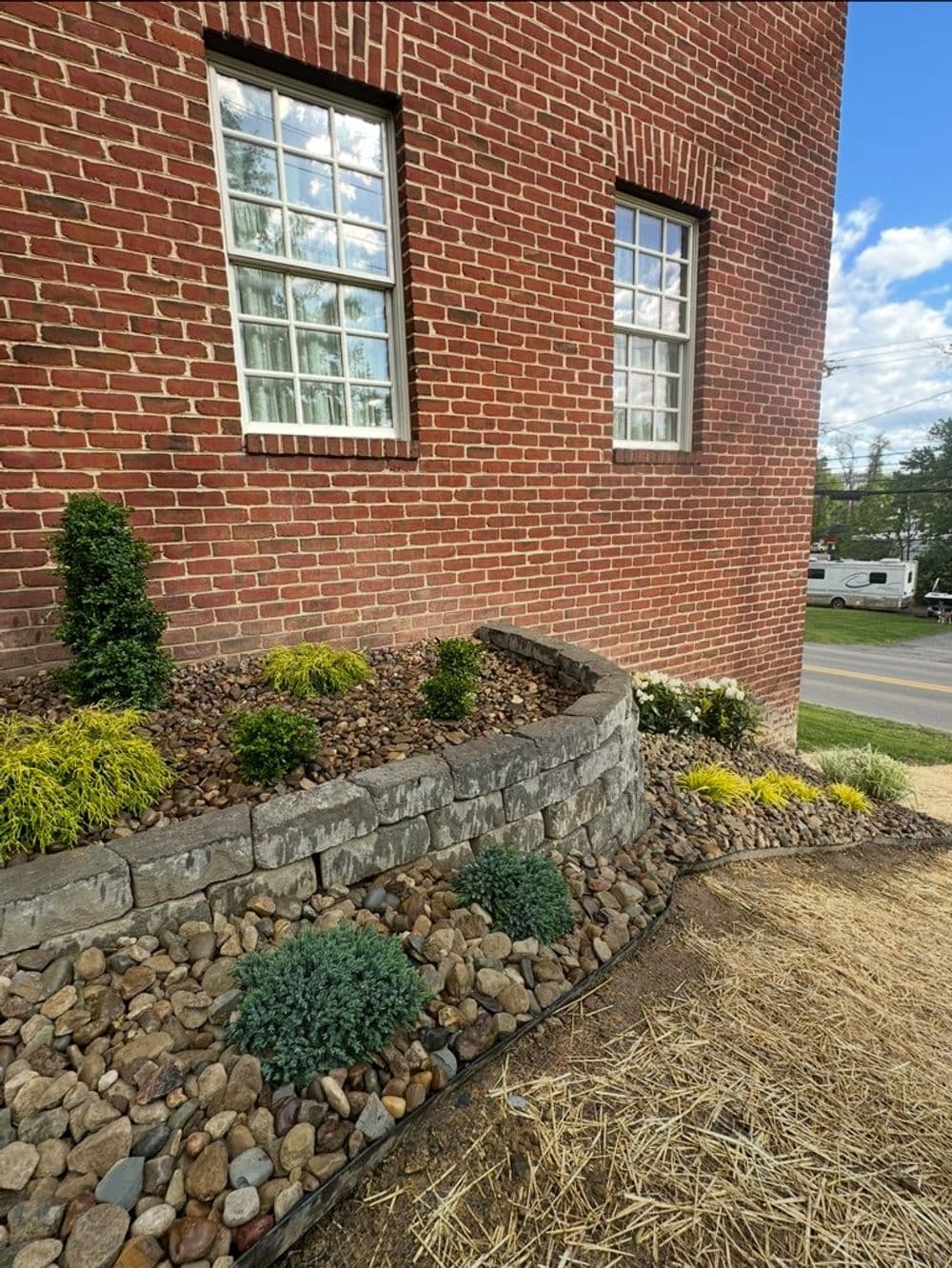 Landscaped stone bed with shrubs near a brick building and windows.